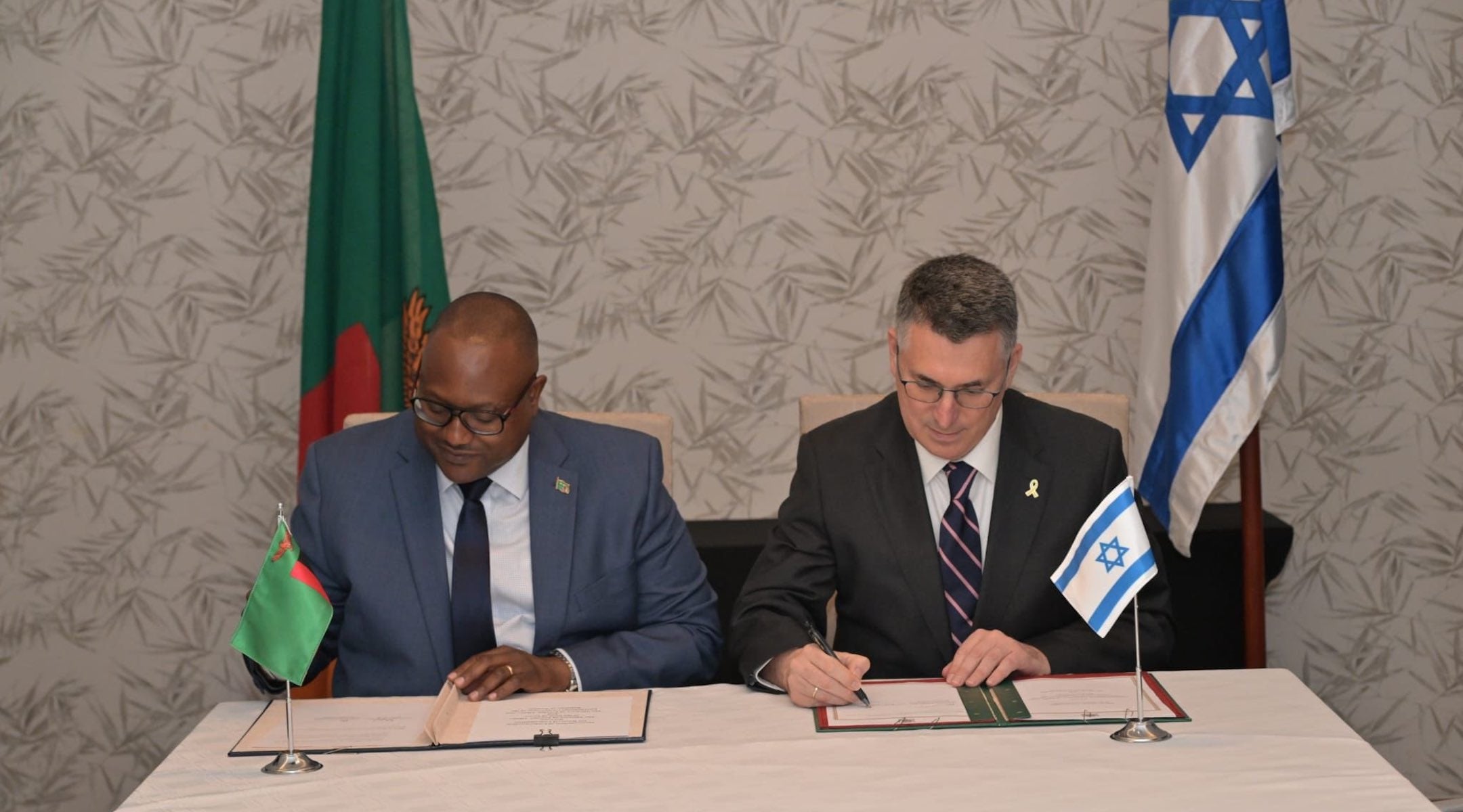 A photo of Zambian Foreign Minister Mulambo Haimbe and Israeli Foreign Minister Gideon Sa’ar signing contracts on a table.